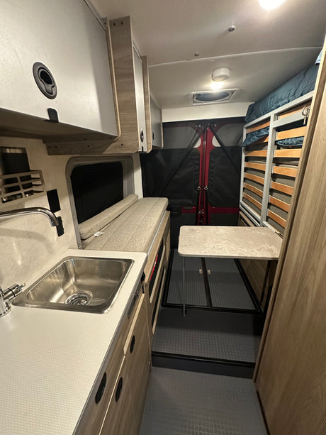 RV rental interior featuring a compact kitchen with sink, convertible bench/bed, dining table, and bunk beds.