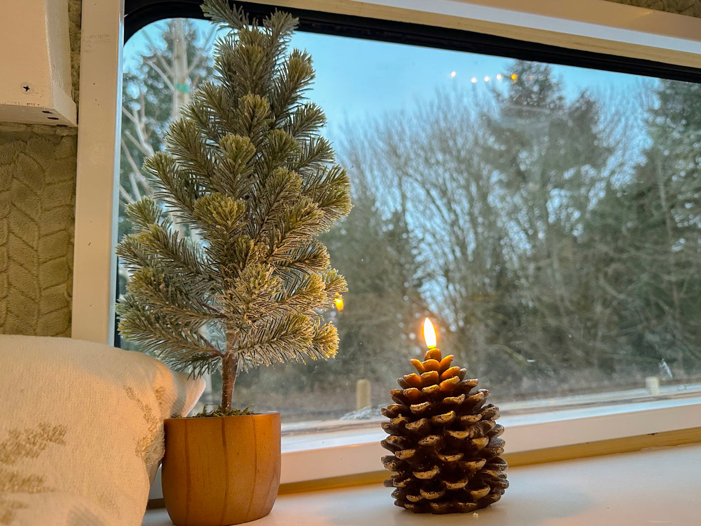 Cozy winter scene in an RV rental: miniature frosted tree & lit pinecone candle on a windowsill.