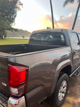 A gray pickup truck, covered in rain droplets, overlooks a serene bay at sunset with palm trees. Perfect for adventure, like an RV rental!