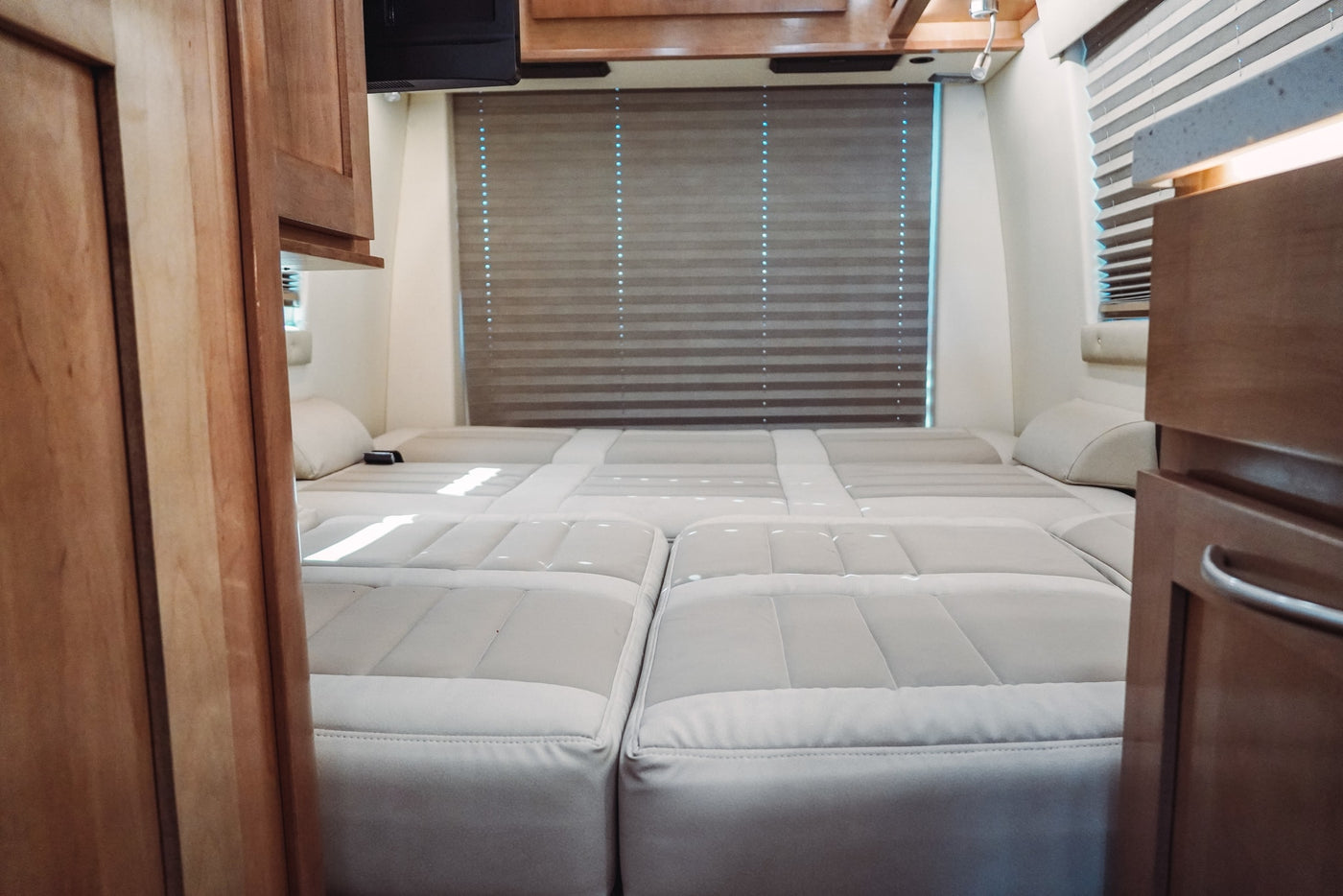 Comfortable RV rental interior featuring a light-colored, modular bed/seating arrangement, wood cabinets, and window blinds. — photo 17