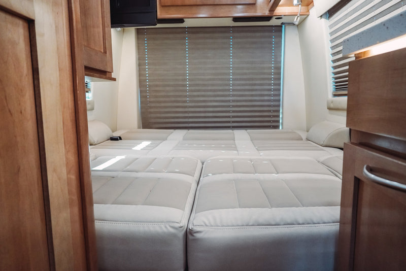 Comfortable RV rental interior featuring a light-colored, modular bed/seating arrangement, wood cabinets, and window blinds. — photo 17
