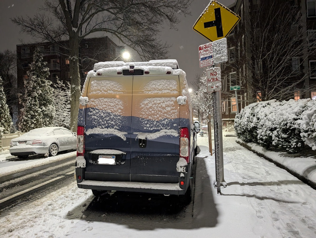 A snow-covered rv rental van parked on a winter city street at night. Snowy trees and street signs complete the scene. — photo 20