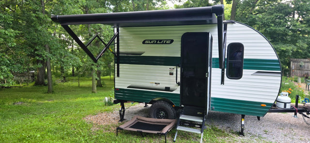 This Sun Lite RV rental features a cozy camper with an extended awning and pet bed, perfect for outdoor adventures in a wooded setting.