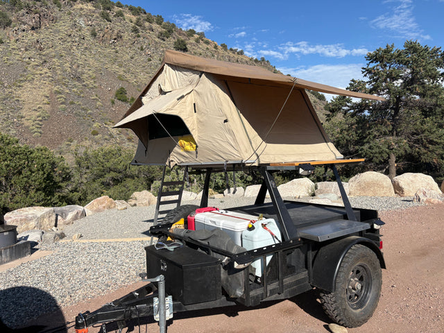 An off-road trailer with a rooftop tent set up for camping, resembling unique RV rental options, against a mountain backdrop.