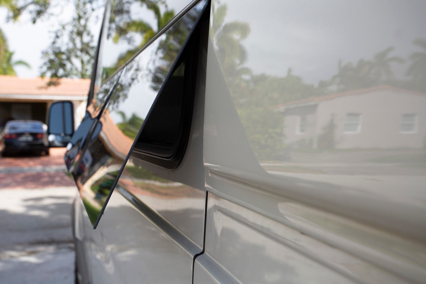 Side view of an RV rental with an open window. Its surface vividly reflects a house & surrounding greenery. — photo 12