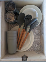 Organized RV rental kitchen drawer: stacked plates, cups, tumblers, and silicone utensils for compact storage.