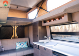 Spacious Moterra **rv rental** interior: modern kitchenette, comfy bench, pop-top, and scenic window view of a river.
