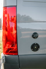 This RV rental van's rear shows a bright red taillight and dual utility hookups for water and power.
