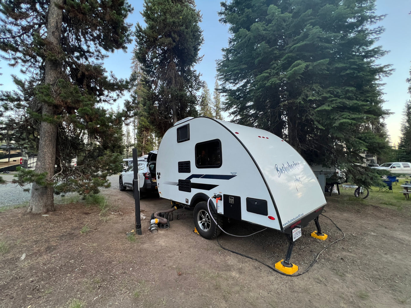 Serene forest campsite with a white Bushwhacker Plus RV rental, fully connected for a comfortable outdoor stay.