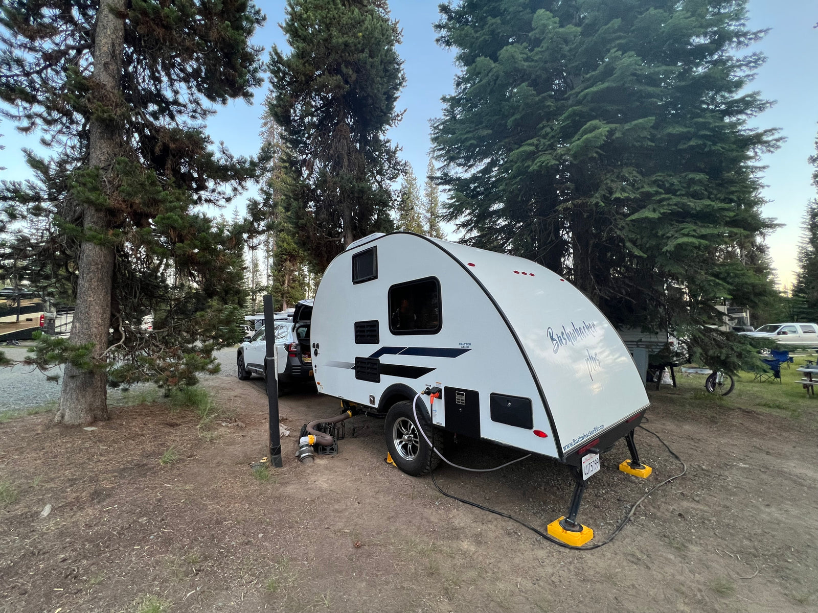 Serene forest campsite with a white Bushwhacker Plus RV rental, fully connected for a comfortable outdoor stay.