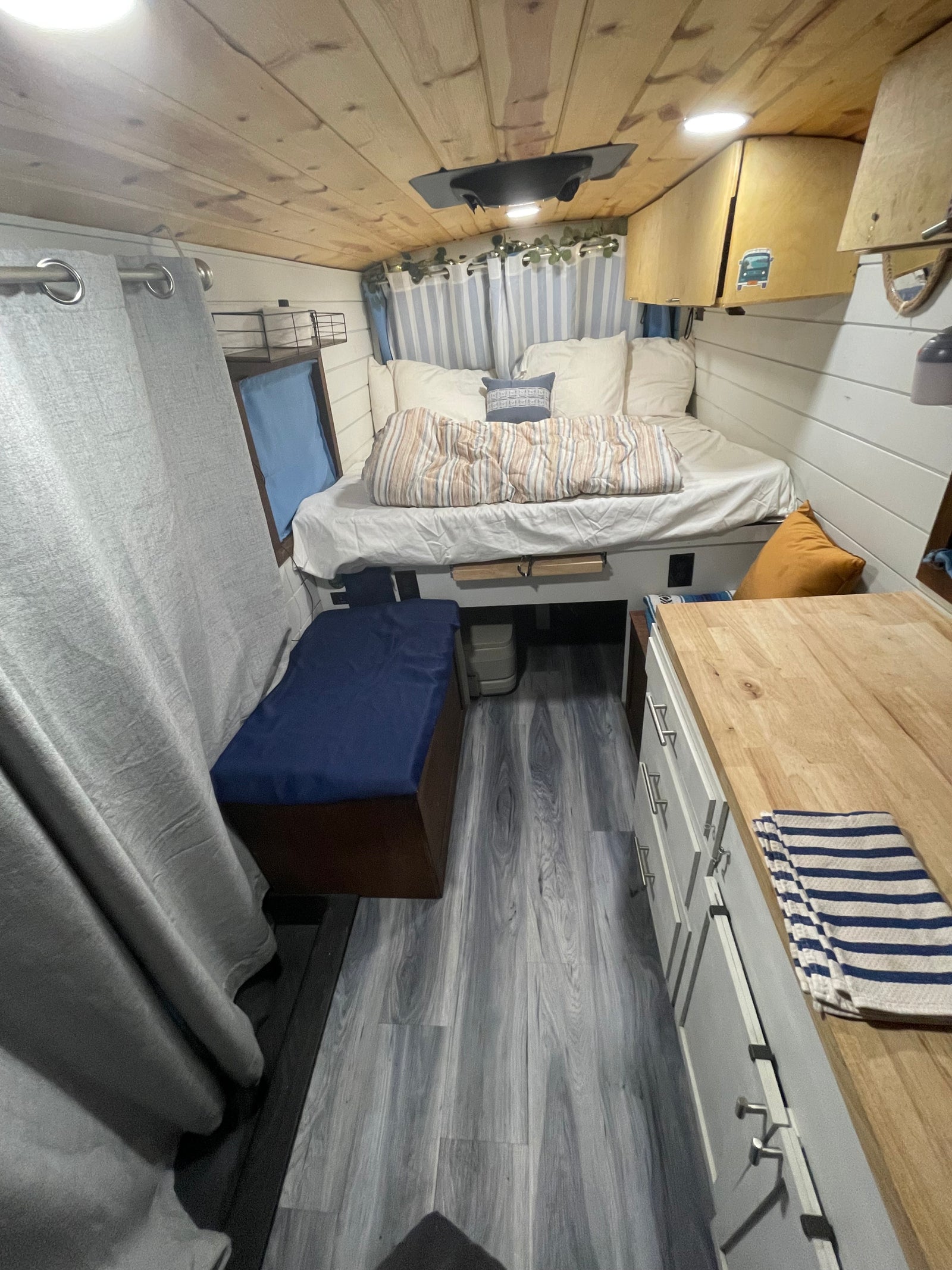 Experience a comfortable rv rental: a cozy bed, warm wood ceiling, and compact kitchen with a butcher block counter.