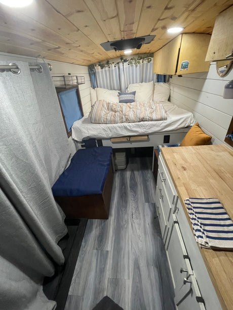 Experience a comfortable rv rental: a cozy bed, warm wood ceiling, and compact kitchen with a butcher block counter.