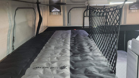 Explore an RV rental's sleeping area: a compact bunk bed with a two-tone gray mattress and safety net for secure, comfortable travel.