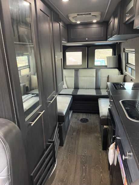 Modern rv rental interior with dark wood cabinets, two-tone gray seating, kitchen, and compact living space for road trips.