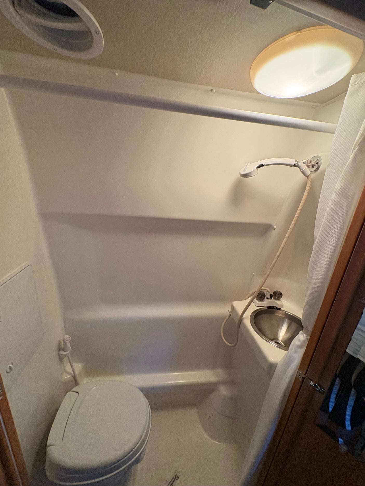 An rv rental wet bath with a toilet, sink, and shower. Includes a ceiling vent and light.
