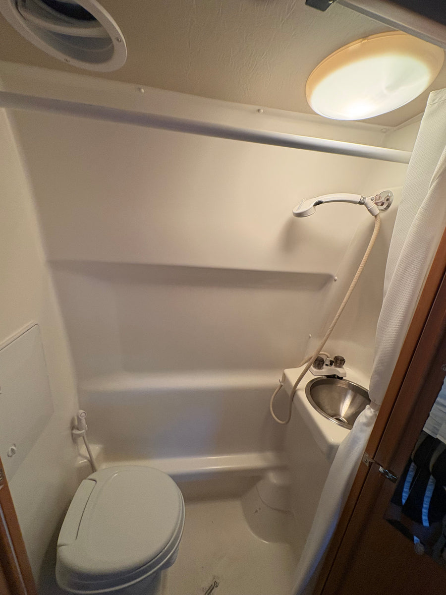 An rv rental wet bath with a toilet, sink, and shower. Includes a ceiling vent and light.