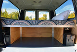 RV rental camper van rear: a patterned bed with under-bed storage, power unit, and tree-lined window views.