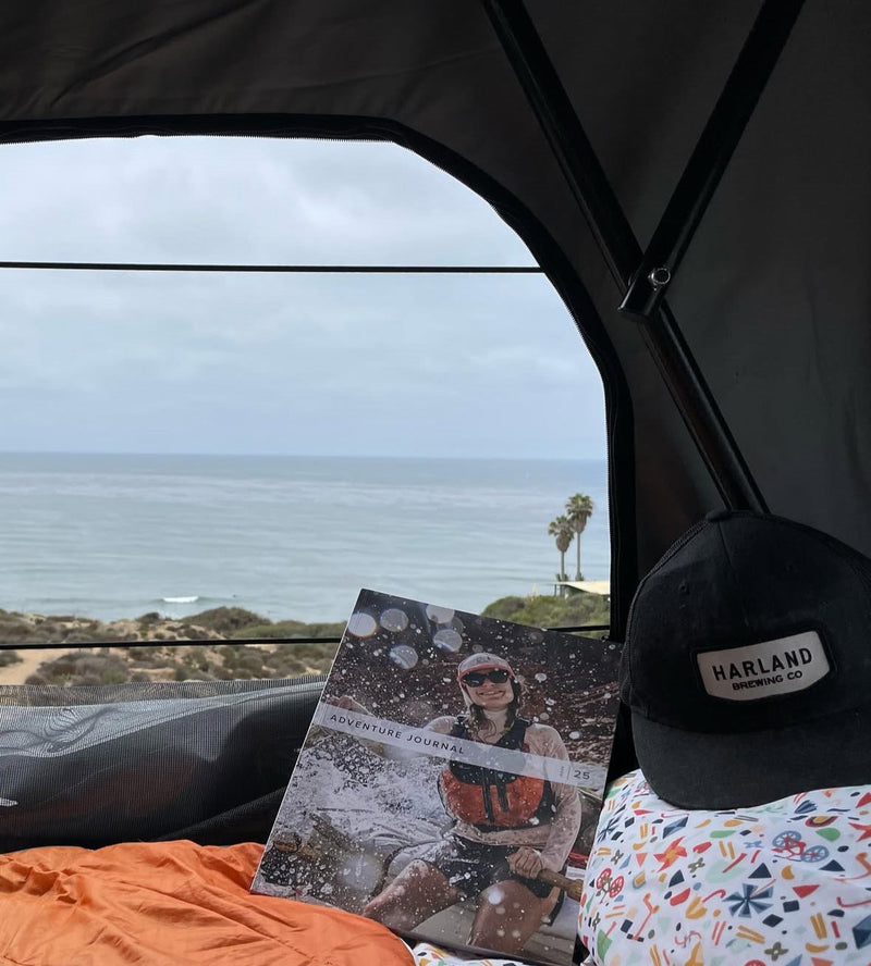 Relaxing in an RV rental overlooking the ocean. Reading an Adventure Journal with a Harland Brewing cap. — photo 17