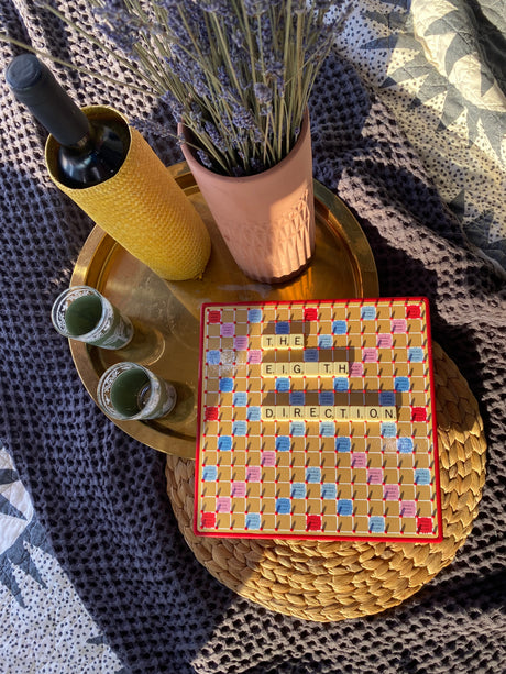 Scrabble spelling 'THE EIGHTH DIRECTION,' wine, and lavender on a tray. A cozy, relaxed setting perfect after an RV rental journey.