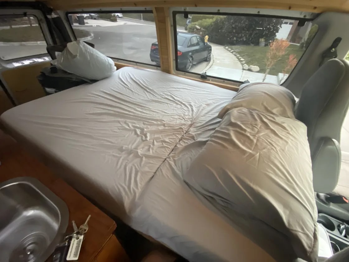  with a sunshade up.|Interior of an RV rental: a converted van with bedding in the back and the driver's cabin visible in front.|Dashboard of an RV rental — photo 8