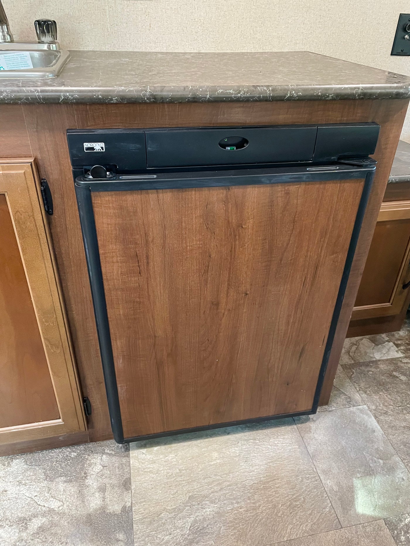 Compact wood-paneled Norcold refrigerator in an RV rental kitchen, integrated under the counter with a sink nearby. — photo 10