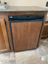 Compact wood-paneled Norcold refrigerator in an RV rental kitchen, integrated under the counter with a sink nearby.