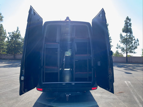 This RV rental van, with rear doors open, shows its custom interior featuring multiple bunk beds for group travel.