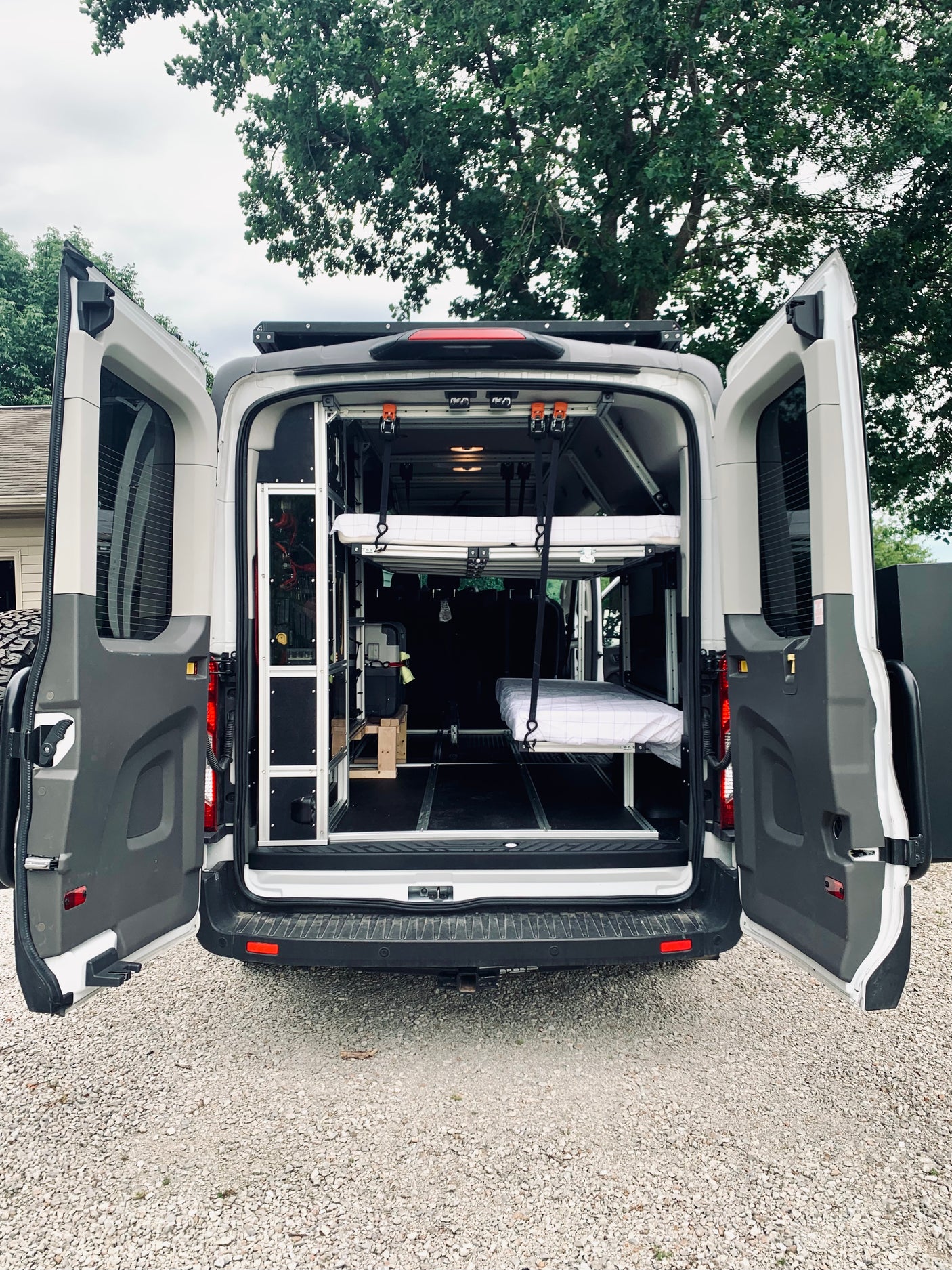 Customized camper van with open rear doors, revealing a versatile interior featuring a suspended bed, storage, and essentials for RV rental.