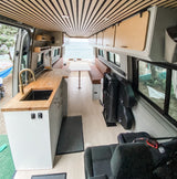 Stunning RV rental: interior of a modern camper van with kitchen, dining area, slatted ceiling, and ocean view.