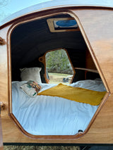 Experience nature in this RV rental: a cozy teardrop camper's interior with a comfy bed and bright window.