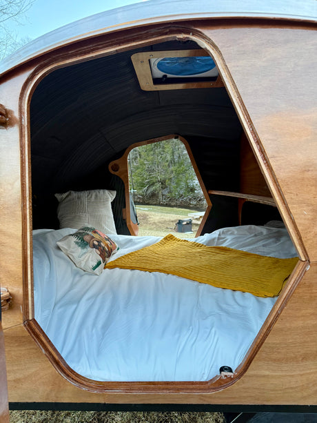 Experience nature in this RV rental: a cozy teardrop camper's interior with a comfy bed and bright window.