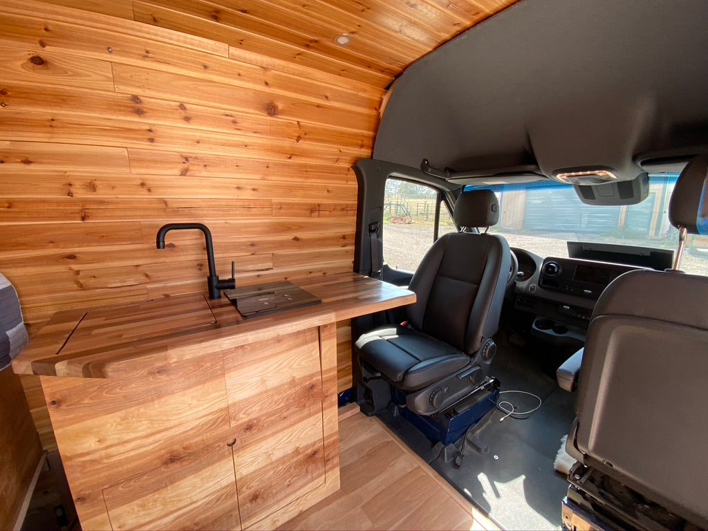 Inside an RV rental: a custom van interior with a warm wood kitchen, modern sink, and spacious front cabin area.