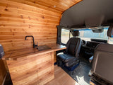 Inside an RV rental: a custom van interior with a warm wood kitchen, modern sink, and spacious front cabin area.