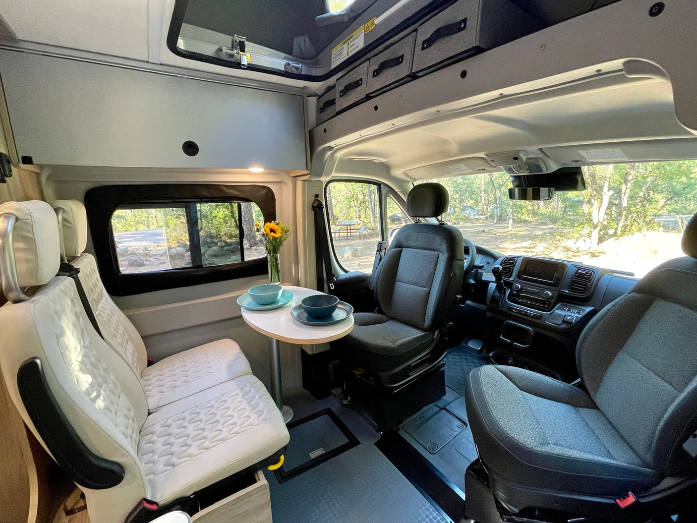 Inside an RV rental: a modern, well-lit camper van interior with front seats, a dining table, and cozy living space.