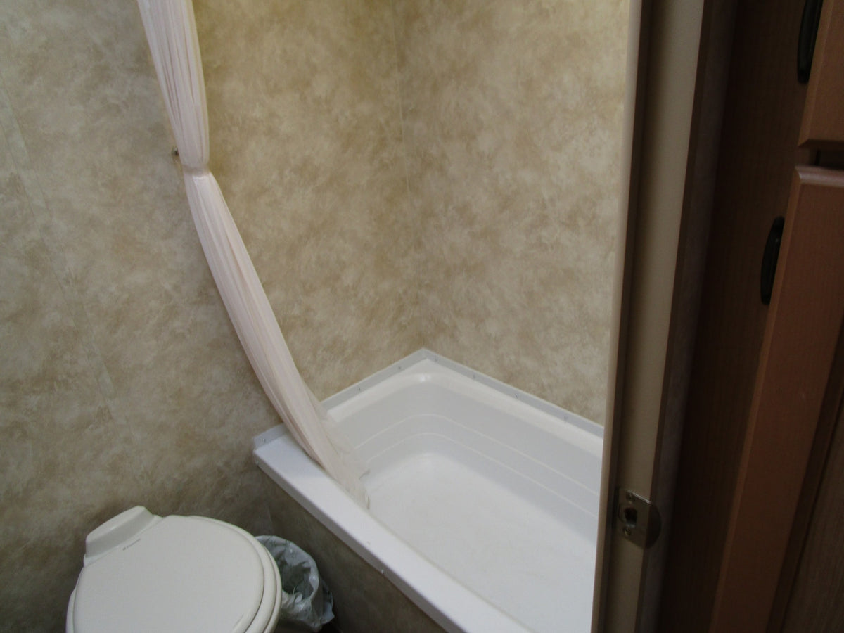 RV rental bathroom with white toilet, tub/shower, and a pulled-back light shower curtain. Practical onboard amenities. — photo 9