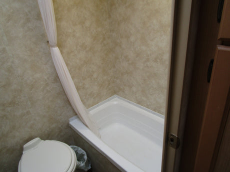 RV rental bathroom with white toilet, tub/shower, and a pulled-back light shower curtain. Practical onboard amenities.