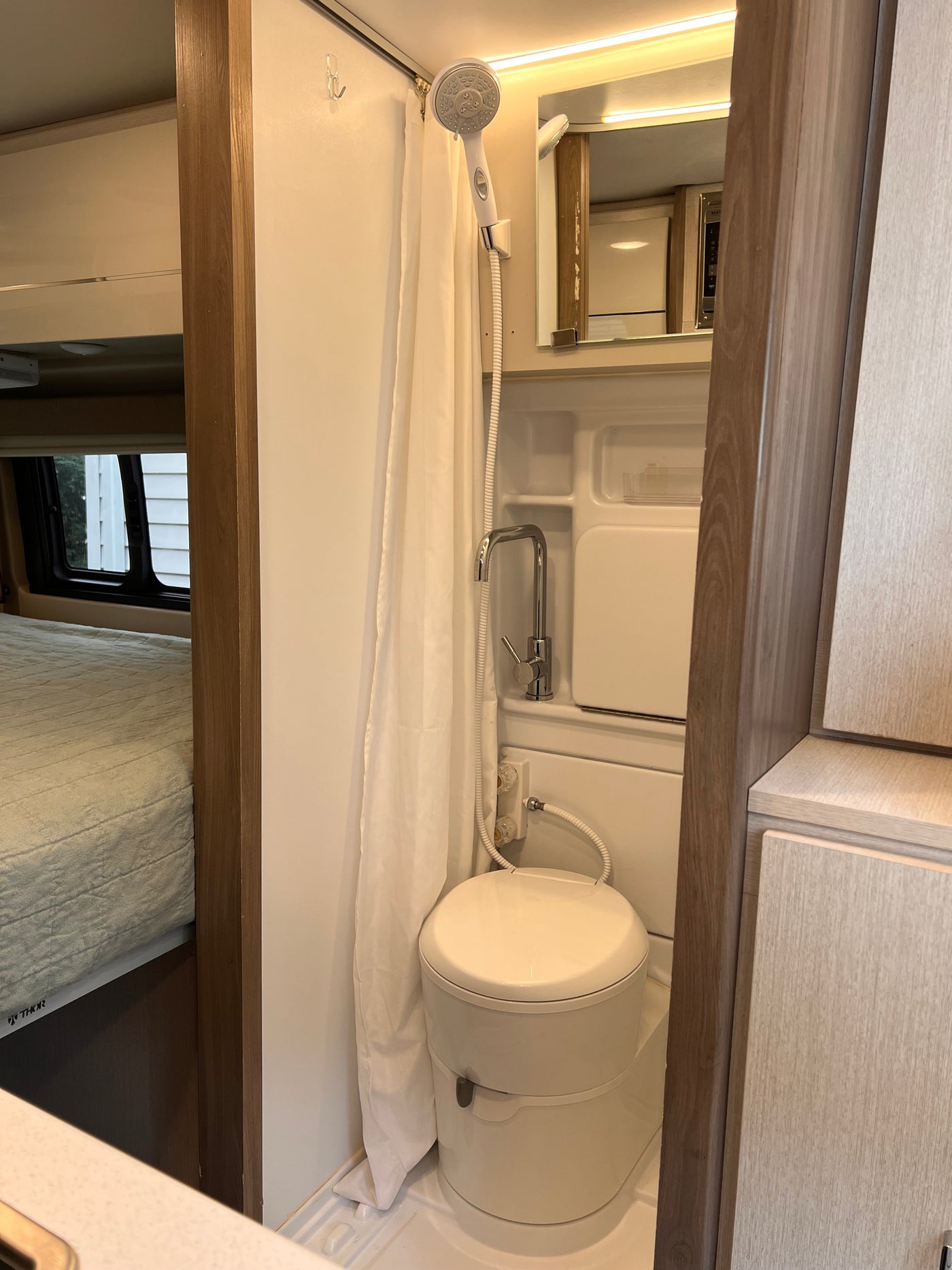 View inside an rv rental: a compact bathroom with shower, toilet, and sink, alongside a comfortable bed area. — photo 7