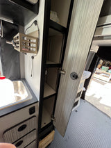 RV rental: Detailed view of a camper van's kitchen area with a sink, open cabinets/shelves, and wall storage.