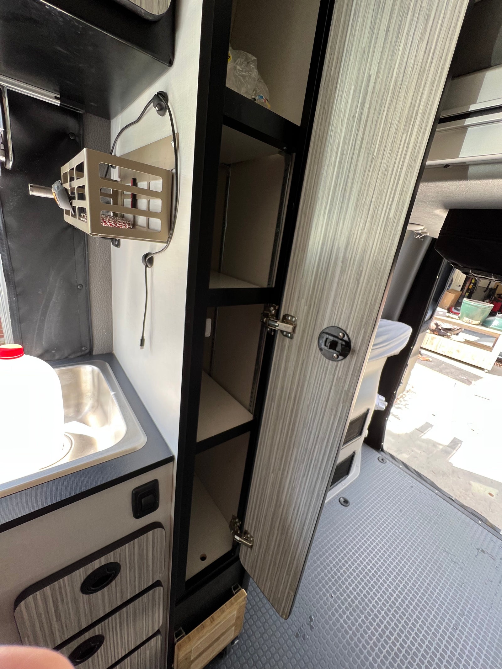 RV rental: Detailed view of a camper van's kitchen area with a sink, open cabinets/shelves, and wall storage.