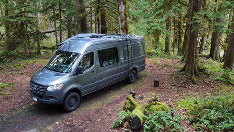 Explore nature with this gray Mercedes Sprinter RV rental, set on a forest path amidst towering, mossy trees.