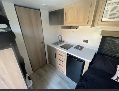 Compact RV rental kitchen with sink, stove, microwave, and mini-fridge, plus an adjacent sleeping area.