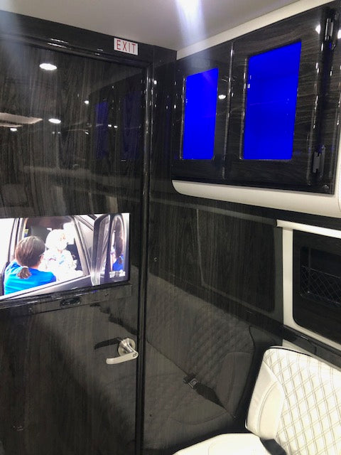 Luxury RV rental interior: sleek dark wood paneling, glowing blue displays, plush quilted seats, and an 'EXIT' sign. — photo 8