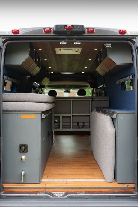 View inside a modern RV rental camper van, showcasing modular bed, storage, wood floor, and overhead compartments.