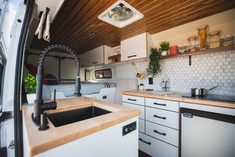Inside a sleek rv rental: modern kitchen with wood counters, sink, stove, fridge, and cozy bed in this custom camper van.