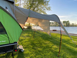 This inviting lakeside scene, perfect for an RV rental getaway, features a green tent and large grey awning by a picnic table.