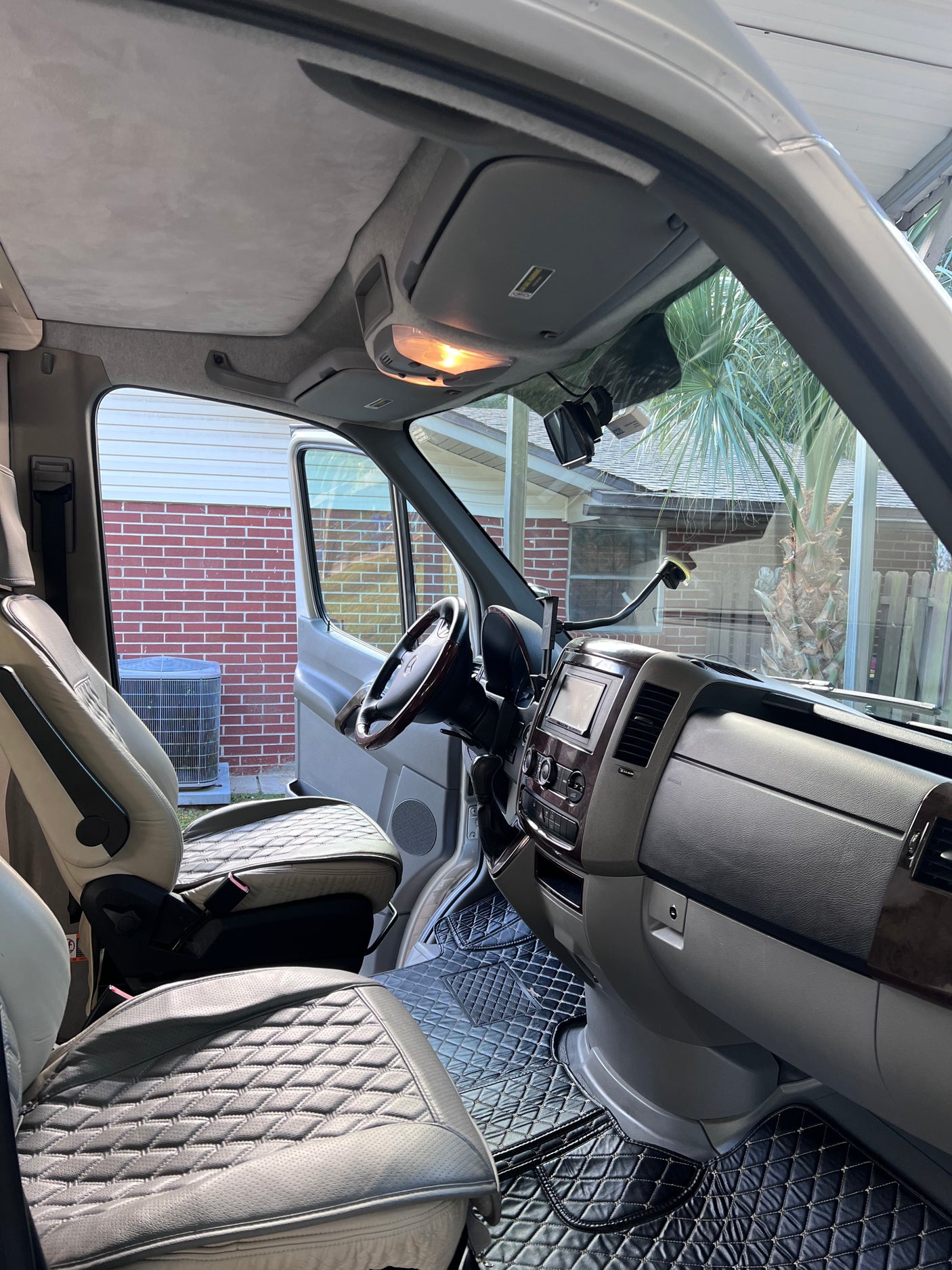 Clean RV rental's front cabin interior. Features bright, quilted leather seats, dashboard, and custom floor mats for travelers.
