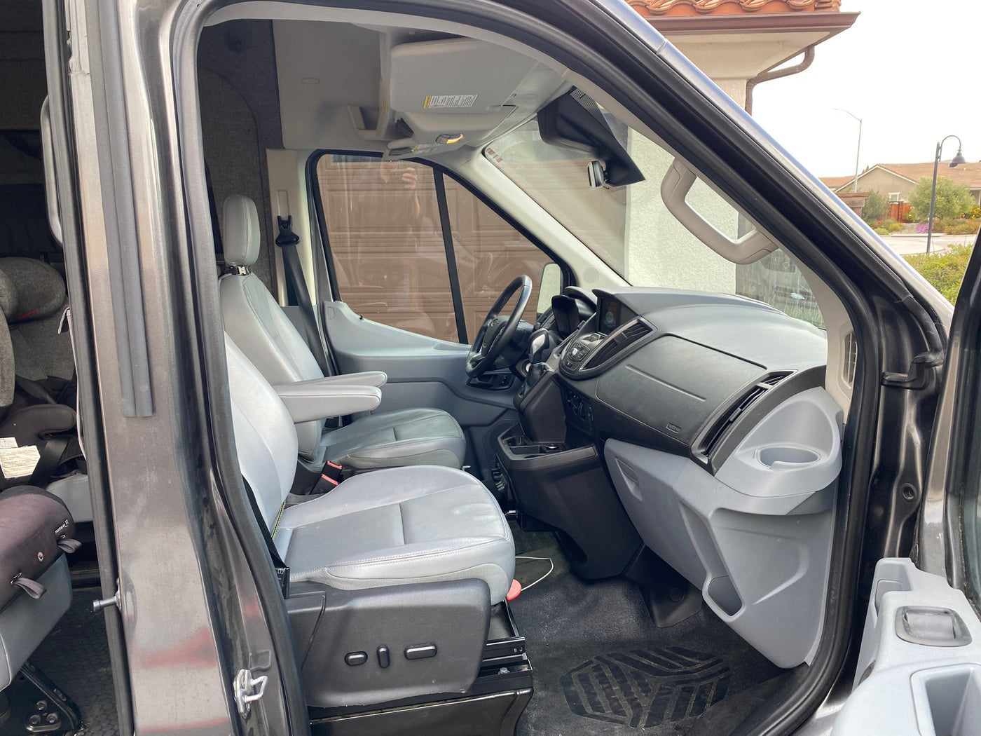 RV rental van's front cabin. View of the driver's seat, dashboard, and passenger area, with a car seat in back. — photo 13
