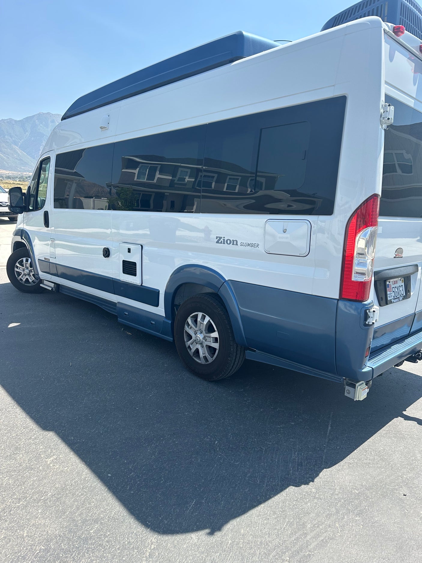 White and blue Zion Slumber RV rental van parked on asphalt, ideal for mountain adventures.