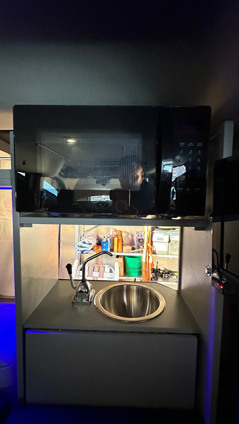 This RV rental features a practical kitchenette with a microwave, sink, storage, and ambient blue lighting. — photo 12