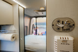 This RV rental interior features a Euroloft bed lift control panel, thermostat, and a serene beach scene visible through the rear.